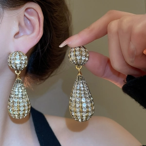 Macro detail of vintage gold drop earrings featuring a hollow frame and sparkling crystals