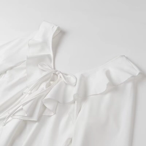 Détail d'une robe blanche à épaules dénudées avec volants et nœud lacé sur tissu doux