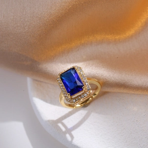 Macro shot of gold ring featuring rectangular blue gemstone and white zircon halo detail