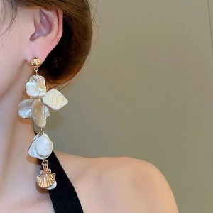 Detailed close-up of long gold fringe earrings with shell accents on model