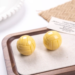 Gros plan détaillé de boucles d'oreilles volleyball en résine jaune sur un plateau
