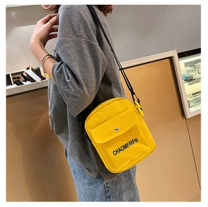 Detail view of a bright yellow canvas crossbody bag featuring black letter print and strap