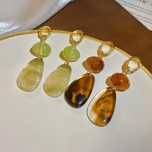 Close-up of geometric resin teardrop earrings in amber and olive green with gold accents