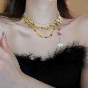 Detail einer mehrlagigen Goldkette mit gelben Perlen und Schmetterlingsanhänger am Model