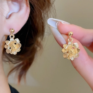 Macro detail of champagne gold floral earrings with textured petals on a model ear
