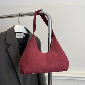 Detailed view of burgundy suede hobo bag with silver bottom studs hanging on a rack