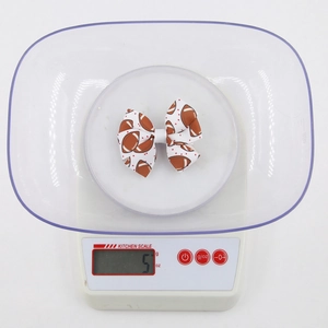 Bow hair clip with football print and red dots on a kitchen scale for weight display