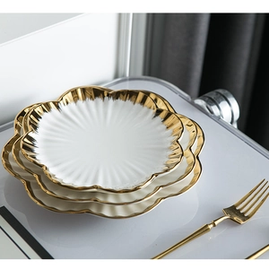 Close-up of stacked white ceramic plates with gold rims and elegant scallop edges