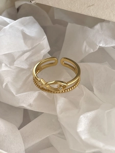 Detail of gold fish-shaped open ring featuring a sparkling central zircon on white paper