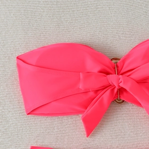 Detail of neon pink bikini top with center bow knot and golden metal ring hardware