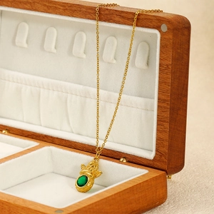 Gold angel pendant necklace with a green gemstone displayed on a wooden jewelry box