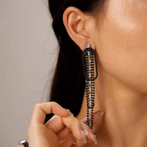 Close-up of long black tassel earrings with rhinestones and round clear zircon studs