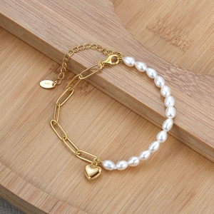 Detail of 925 silver bracelet with baroque pearls and gold heart pendant on wood