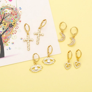 Close-up of golden earrings with cross, moon, and devil eye designs on decorative card