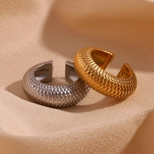 Macro detail of gold and silver C-shaped earrings with scale texture on satin
