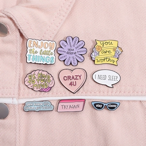 Detailansicht von neun bunten Emaille-Pins mit Motivationssprüchen auf rosa Denim