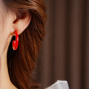 Close-up of elegant glossy red C-shaped hoop earrings worn by a female model