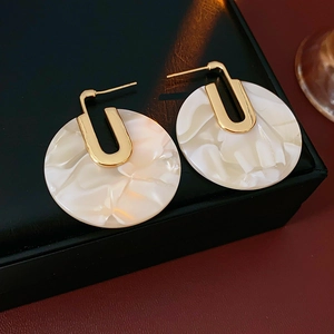 Detail view of round white marble acetate earrings with gold plated U-shaped metal clasps