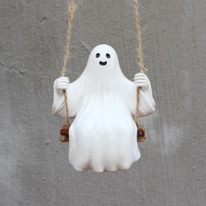Detail of white ghost figurine sitting on a wooden swing with hemp rope for Halloween garden