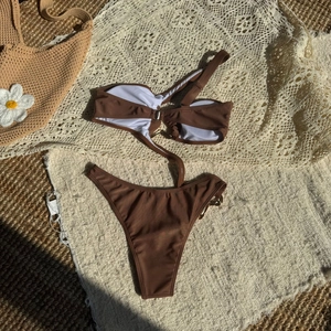 Flat lay of brown bikini with metal ring detail on straw mat and lace beach background