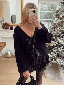 Détail d'un gilet noir à col en V avec trois nœuds à paillettes et une maille douce et ample