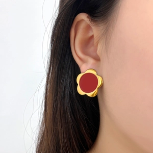 Close-up of elegant gold flower stud earrings with red center worn by a female model