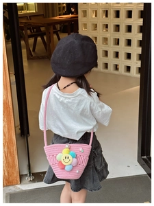 Pink woven kids crossbody bag with large floral smiley face shown on a model