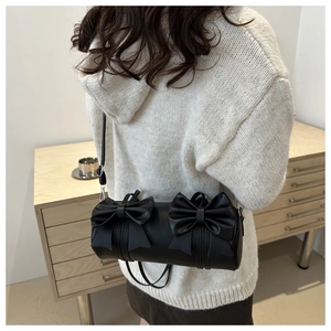 Detail of black cylindrical shoulder bag with double bows and adjustable strap
