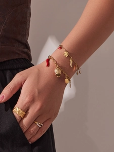 Détail de bracelets dorés avec pendentifs piment rouge et cloche avec bagues sur un mannequin
