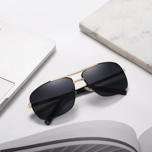 Detail of square pilot sunglasses with gold double bridge frame on a white desktop