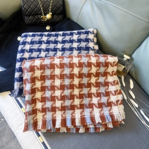 Detailed view of houndstooth scarf texture with thick fringes on a soft blue sofa background
