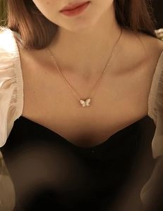 Close-up of golden titanium necklace with white mother-of-pearl butterfly pendant on neck