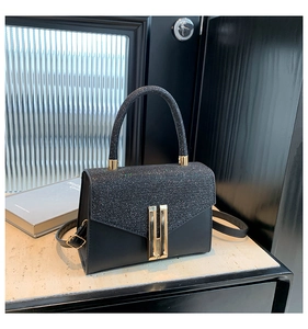 Close-up of black handbag featuring shimmering sequin flap and iconic golden H-clasp detail