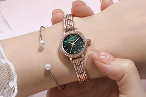 Close-up of rose gold watch with green malachite dial and pearl bracelet set on wrist