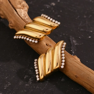 Dettaglio di orecchini ad ala placcati oro 18K con zirconi bianchi su legno naturale