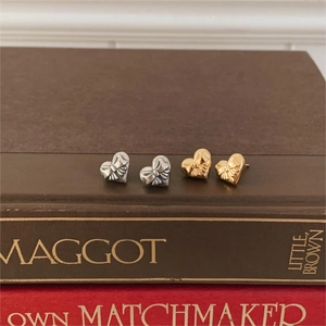 Close-up of heart-shaped bow stud earrings in vintage silver and bright gold finishes