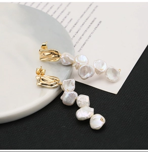 Detail of long gold earrings featuring baroque pearls and irregular metallic tassels