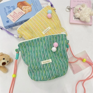 Detail showing knit texture and colorful pom-poms of adjustable crossbody phone bags