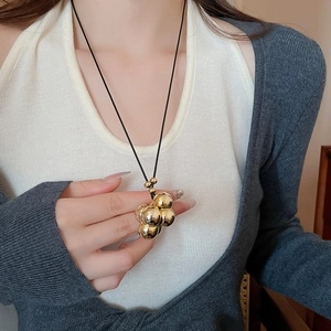 Dettaglio ravvicinato di un ciondolo a grappolo di sfere dorate su una collana nera