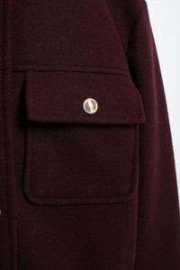 Dettaglio della tasca con patta su un cappotto di lana bordeaux con bottone in metallo