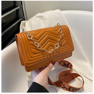 Detail of orange quilted crossbody bag with golden floral chain and patterned strap