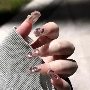 Close-up of translucent coffin nails featuring pink-purple glitter and 3D crystal stones