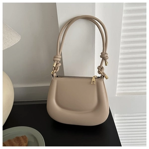 Close-up of beige shoulder bag with quilted panel, knotted strap and gold hardware accents