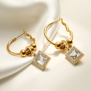 Gold geometric earrings with square zircon pendants on soft white silk fabric background