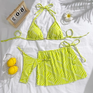 Flat lay of neon green wave pattern 3-piece bikini set with pearl chain and beach decor