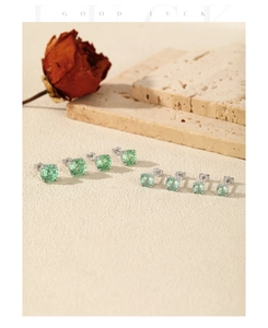Macro shot of eight green gemstone stud earrings with silver bases on a stone surface