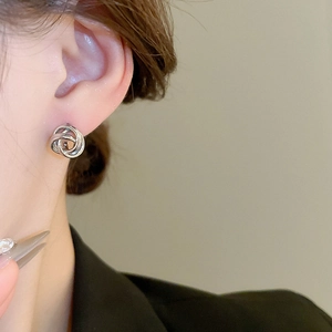 Close-up of a silver minimalist twisted knot stud earring worn by a model in a side view