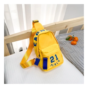 Détail du sac bandoulière enfant en nylon jaune avec imprimé lettres bleues sur lit