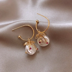 Detail of gold C-shaped earrings with large white pearl and red gemstone accent on silk