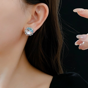 Close-up of blue-green crystal stud earrings with pavé halo setting on female model